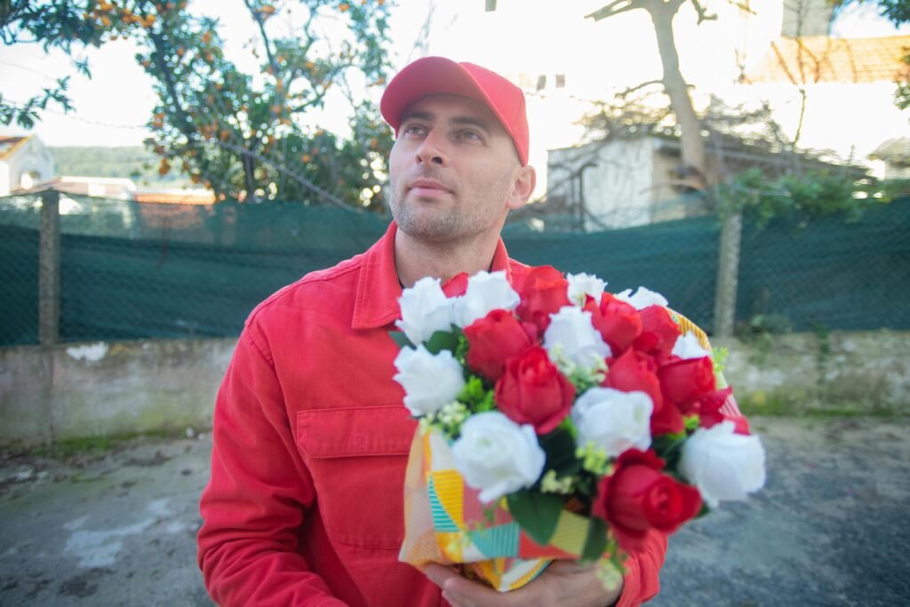 A delivery man in a red uniform holding a bouquet of red and white roses outdoors in Portugal.